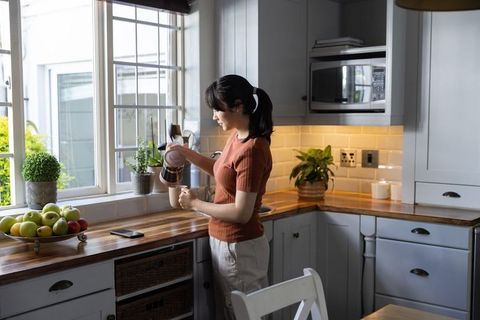 Asian woman in thirties pouring french press coffee in bright cozy modern kitchen