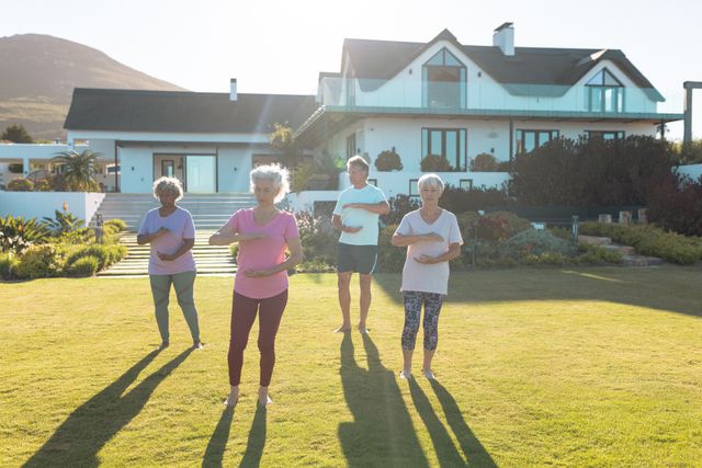 Group of senior friends engaging in outdoor exercise on a sunny day in front of a nursing home. Ideal for promoting active lifestyles, wellness programs, assisted living facilities, and community support for seniors. Useful for websites, brochures, and advertisements related to senior care, fitness, and retirement living.