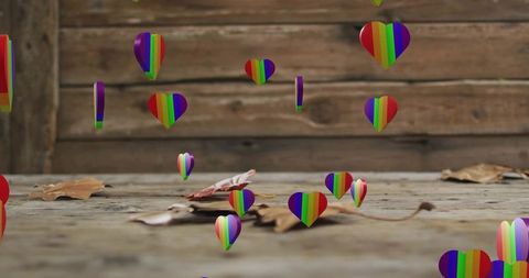 Hovering rainbow hearts drifting above rustic wood plank table with dried leaves