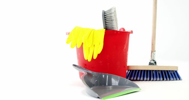 Cleaning equipment, including a red bucket with yellow gloves, a broom, and a dustpan, is arranged against a white background, with copy space. These tools are commonly used for household chores and maintaining cleanliness in various settings.
