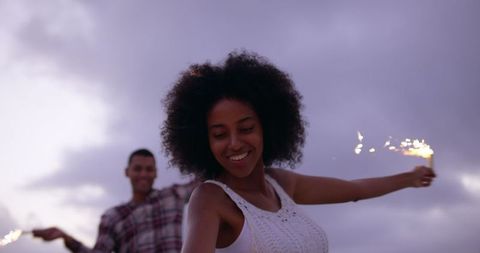 Joyful biracial couple dancing with sparklers on beach at dusk