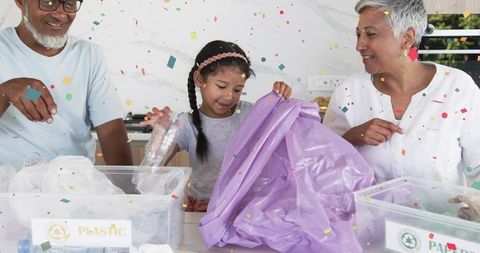 Grandparents teaching child recycling by sorting plastic and paper on kitchen counter