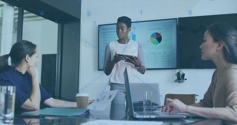 Woman leading executive team presentation in modern boardroom using tablet and data charts