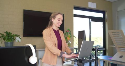 Businesswoman standing and working at adjustable laptop stand in modern bright office