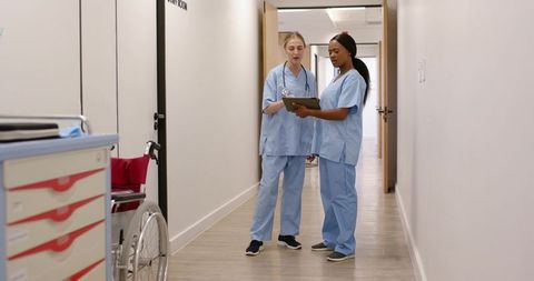 Multiracial nurses consulting on tablet in hospital corridor wearing blue scrubs