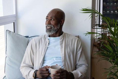 Senior african american man relaxing on window seat with coffee, serene home lifestyle