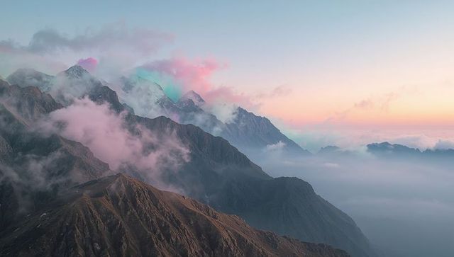 Rugged alpine ridge rising through mist and pastel clouds at dawn panorama
