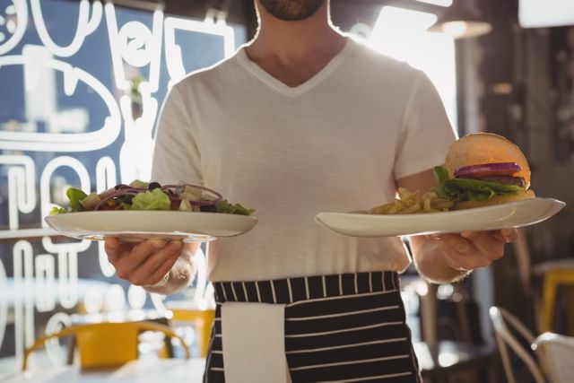 Waiter holding plates with salad and burger in a cafe. Ideal for illustrating restaurant service, dining experiences, and hospitality industry. Useful for food blogs, restaurant websites, and marketing materials for cafes and eateries.