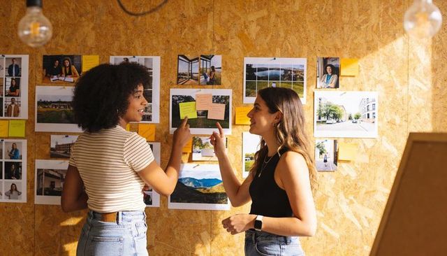 Designers collaborating while pointing at moodboard with prints and sticky notes