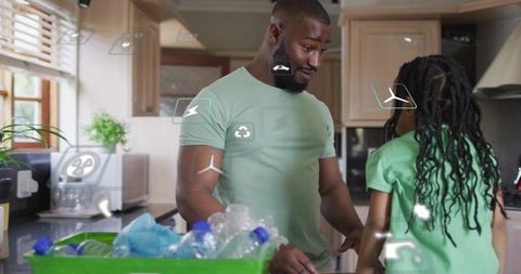 Father and daughter teaching recycling at kitchen counter with green bin and eco icons