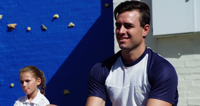 Male instructor interacting with young schoolchildren during an outdoor fitness activity. The image is perfect for advertising educational programs, sports camps, or community activities promoting physical fitness and mentoring.