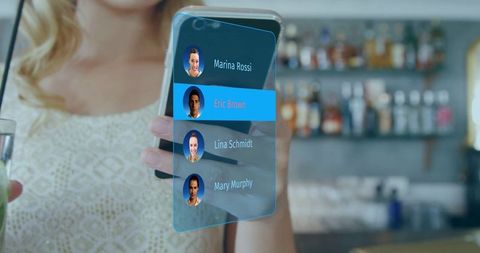 Woman holding smartphone at bar viewing holographic contact list with avatars and cocktail