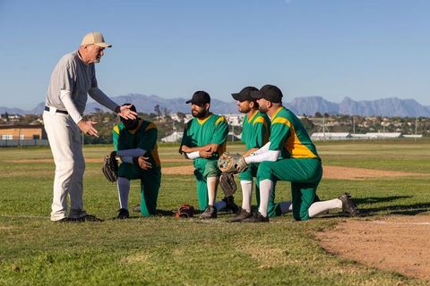 Senior Coach Giving Instruction During Baseball Infield Huddle With Kneeling Players