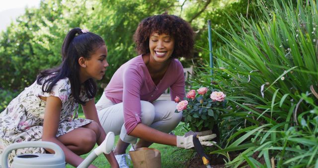 Happy african american mother and daughter, taking care of plants outdoors. staying in garden in isolation during quarantine lockdown