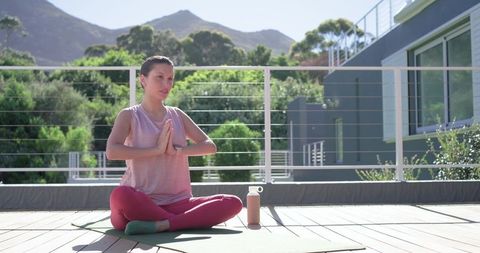 African american woman practicing sunrise yoga on modern terrace with water bottle