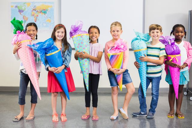Group of cheerful children standing in classroom, each holding a colorful gift cone. Ideal for educational materials, back-to-school promotions, and celebrating diversity in education.