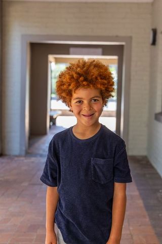 Smiling african american boy with curly red hair standing in sunlit entryway