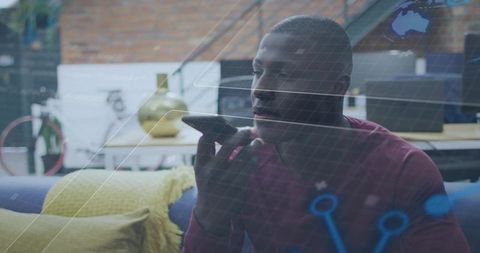 Man using voice assistant on smartphone in cozy loft workspace with blue digital overlay