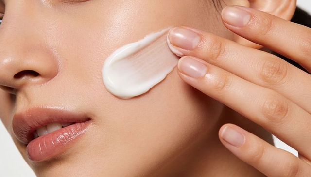 Asian woman applying moisturizer to cheek closeup for skincare hydration and glow
