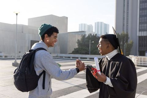 Sunlit graduation celebration with diverse friends shaking hands on urban rooftop plaza