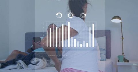 Woman sitting on bed holding lower back with hud health dashboard and smartphone nearby