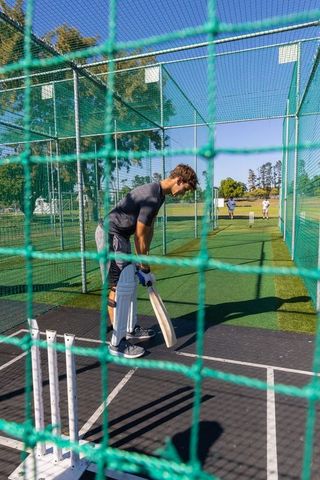 Young batsman practicing in outdoor cricket nets wearing pads and gloves