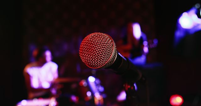 Scene captures closeup of microphone on stage with live band in background, offering an electric atmosphere suitable for event promotions, music marketing, or concert advertisements.