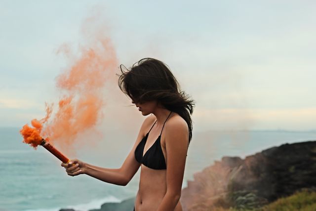 Young Woman in Bikini Holding Orange Smoke Flare by Seaside - Download Free Stock Photos Pikwizard.com