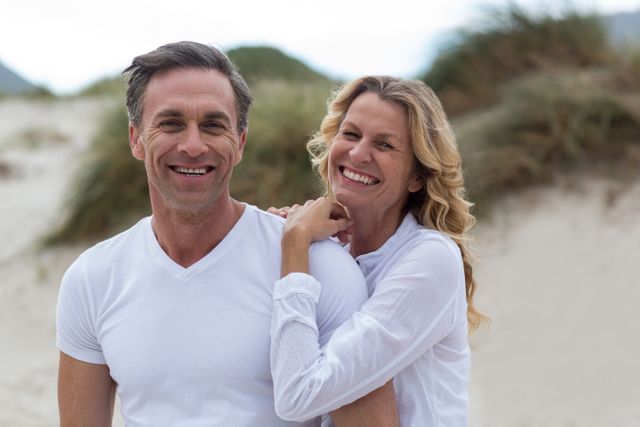 Mature couple smiling and enjoying their time together on the beach. Perfect for use in advertisements promoting healthy lifestyles, vacation packages, relationship counseling, and outdoor activities. Ideal for illustrating themes of love, happiness, and relaxation.