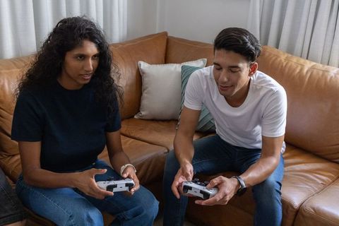 Young couple playing video games on leather sofa with white controllers and casual jeans