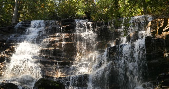Sunlight filters through the trees, casting a serene glow on the cascading waterfall, with copy space. The natural beauty of the waterfall creates a tranquil and refreshing atmosphere.