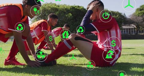 Kneeling soccer players receiving field care wearing red kits and orange bibs with green eco icons