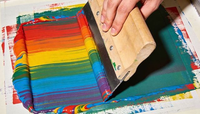 Artist using squeegee pulling rainbow ink across screen for vibrant screen printing