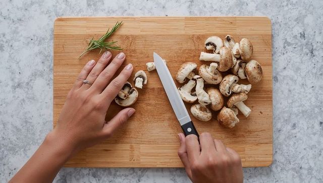 Top-down chopping brown mushrooms by female hands on wooden cutting board with rosemary