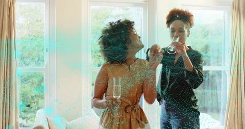 Two women chatting holding wine and champagne flutes in bright home interior
