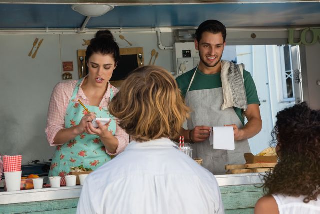Food truck owners taking orders from customers, showcasing a vibrant street food scene. Ideal for use in articles about small businesses, food services, urban dining, and customer interactions.