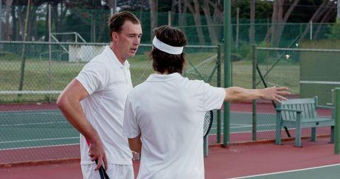 Tennis partners discussing strategy on outdoor hard court wearing white athletic outfits