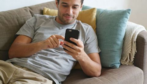 Young man relaxing on couch scrolling smartphone, casual home leisure and daily connection
