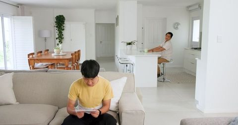 Father observing son reading letter in bright family room