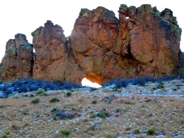 This image depicts a striking rock formation in a desert environment. The clear sky highlights the rugged terrain, emphasizing the natural arch within the rocks. Suitable for use in travel brochures, geology publications, nature documentaries, and educational materials about natural landscapes and geological formations.