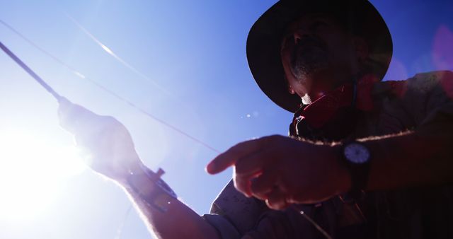 Silhouette of a man casting a fishing rod under bright sunlight. Ideal for themes related to outdoor activities, adventure, fishing enthusiasts, and recreational hobbies. Can be used in articles about fishing techniques, promotional materials for fishing gear, or visuals for relaxation and nature exploration.