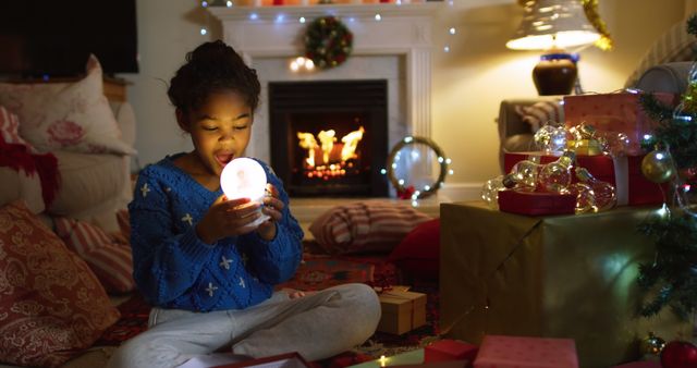 There is a young child sitting in a cozy living room, surrounded by festive Christmas decorations, a fireplace, and presents. This image captures the joyful anticipation and magic of the holiday season. Ideal for use in holiday advertisements, promotions, greeting cards, and social media posts celebrating family and festive traditions.
