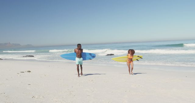 Happy biracial couple carrying surfboards walking on sunny beach - Download Free Stock Photos Pikwizard.com