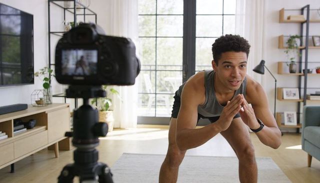 Home fitness instructor filming live workout in bright living room with dslr and tripod