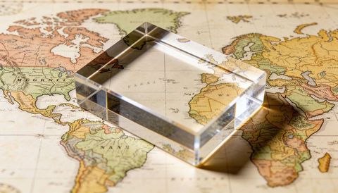 Crystal block magnifying vintage world map, prism highlights over antique atlas