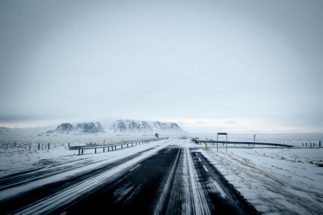 Depicts a desolate winter road cutting through a snowy landscape with distant mountains in the background. Ideal for use in travel blogs, climate articles, or scenic journey advertisements. Highlights the beauty and isolation of winter landscapes.