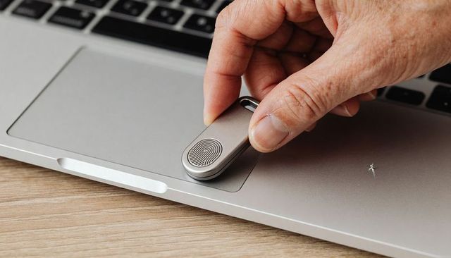 Placing fingerprint usb security key on silver laptop trackpad with hand and scuff