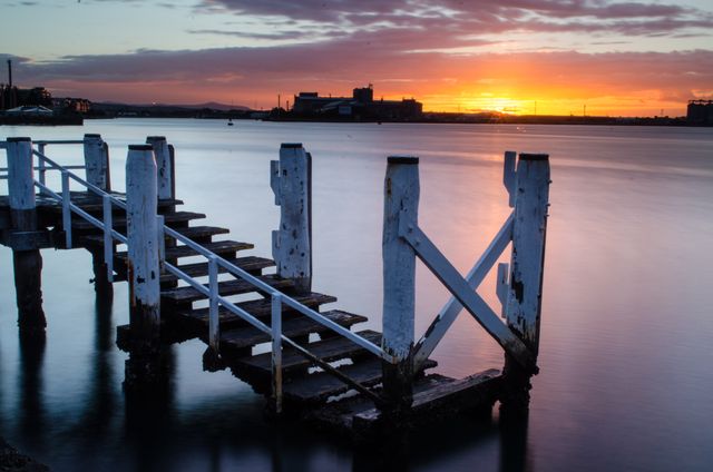 Beautiful scene of broken pier extending into calm waters under colorful sunset sky. Ideal for backgrounds, nature-themed designs, and travel promotion materials.