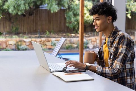 Young man enjoying remote work outdoors with laptop and coffee