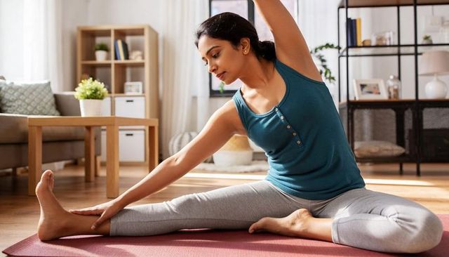 Indian woman practicing seated side stretch on yoga mat in bright modern living room